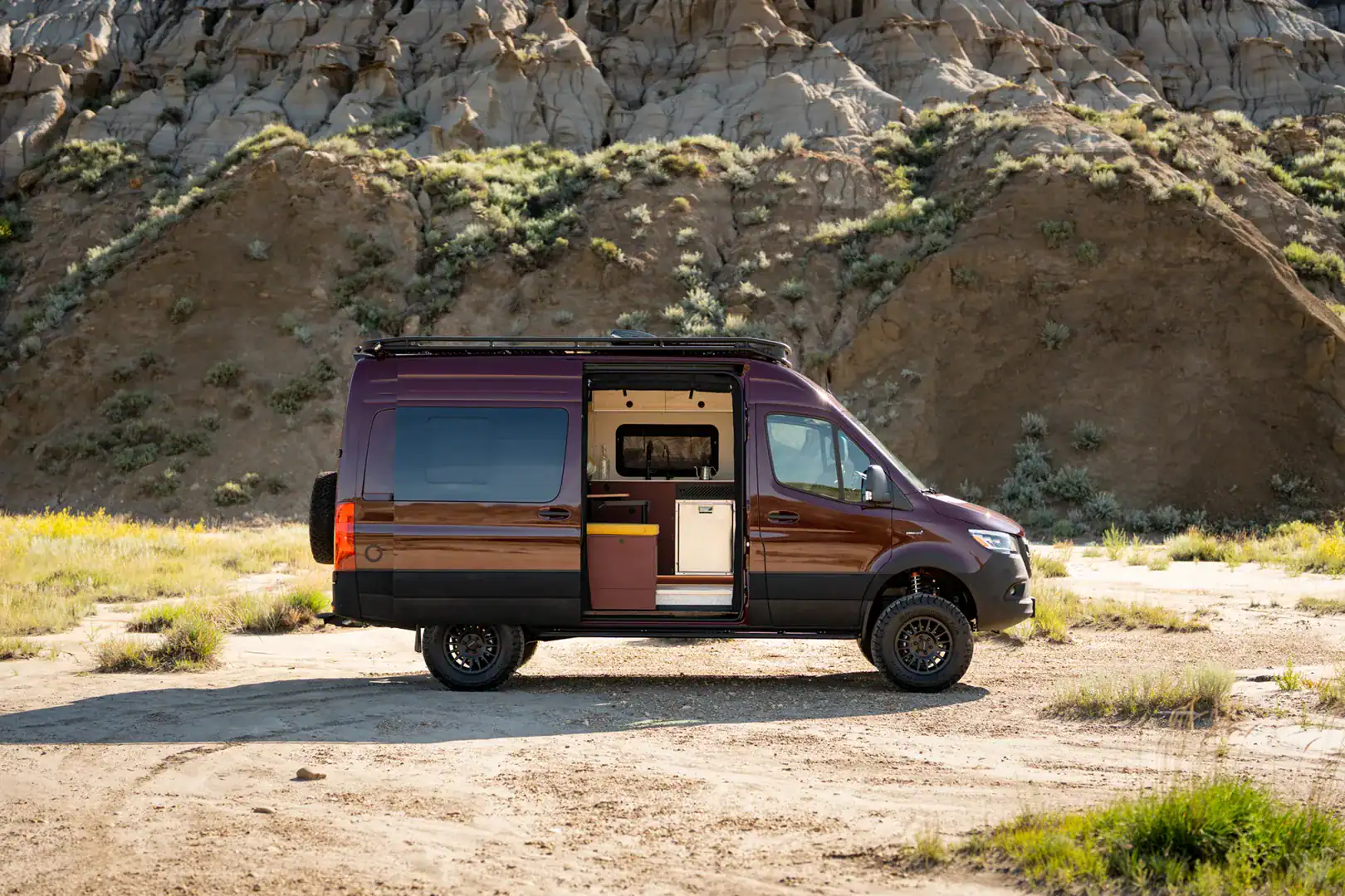 The Yama Vans Brio, a two-tone purple and bronze Mercedes Sprinter 144 camper van, parked in the badlands with its sliding door open