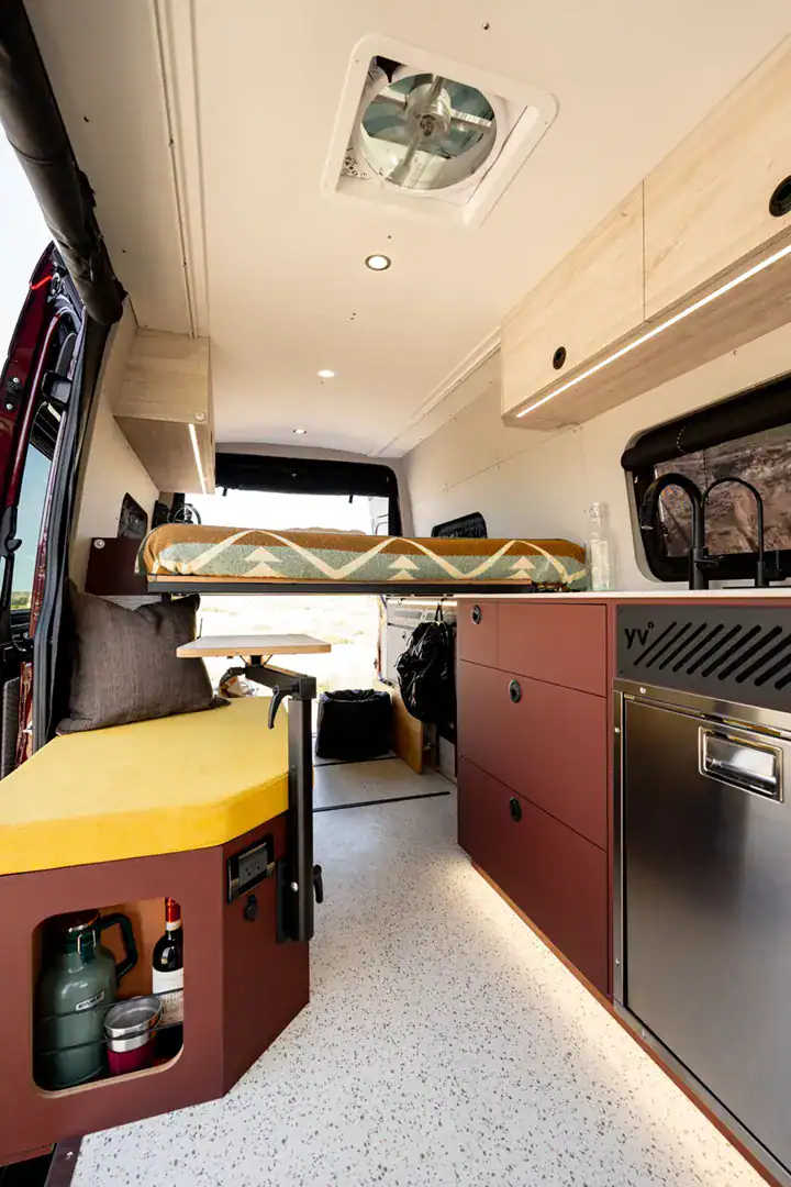 The warm terracotta and maple galley of the Yama Vans Brio with a cooktop, sink, and pull-out seat