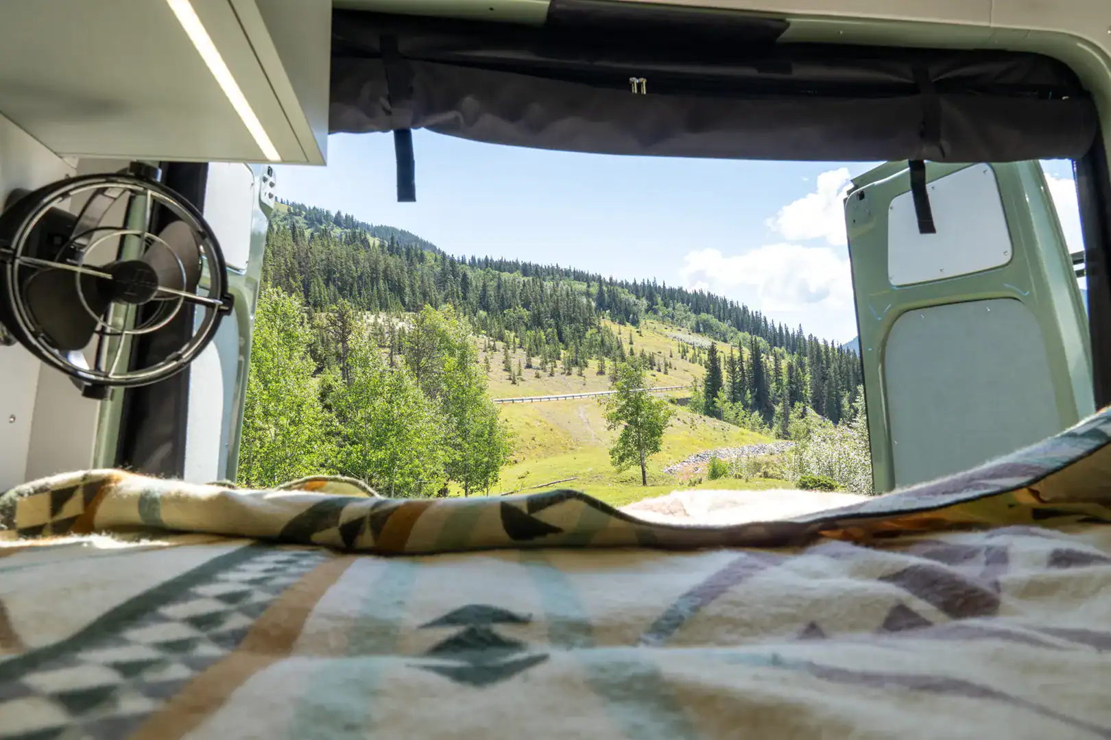 The rear lengthwise bed of the Yama Vans Fitz with a Pendleton blanket and a mountain view through the window