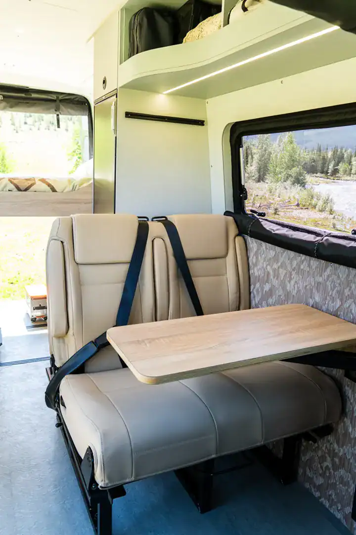 The dinette in the Yama Vans Fitz with cream leather seats and a wood table