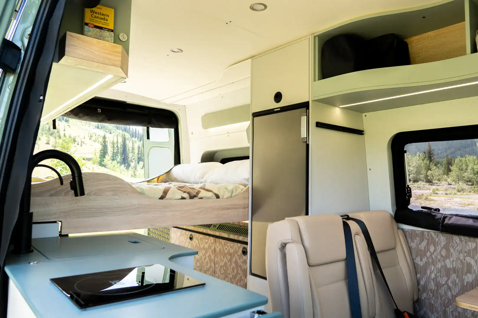 The bright, lake-toned interior of the Yama Vans Fitz with pale counters, maple cabinetry, and a rear bed