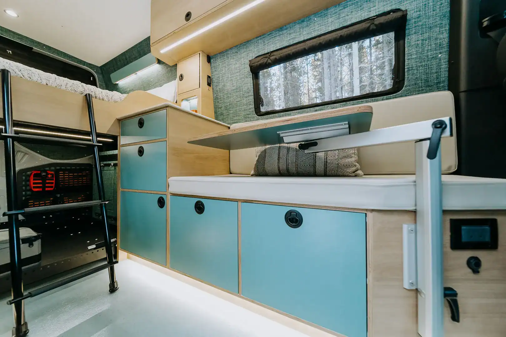 The lengthwise bed and gear garage at the rear of the Yama Vans Furō with teal cabinetry