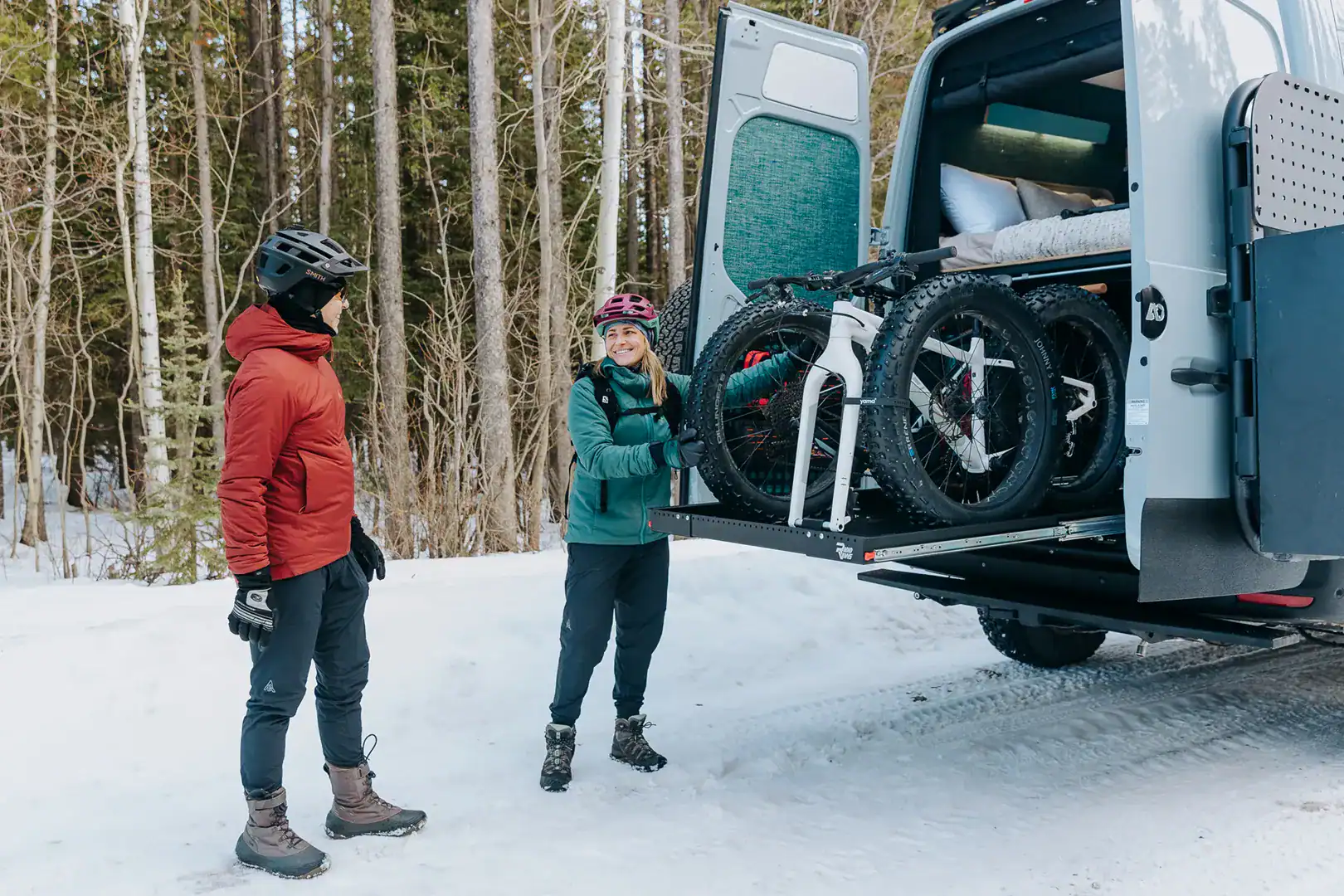 Two mountain bikes mounted on the swing-out rear rack of the Yama Vans Furō with the owners in winter gear