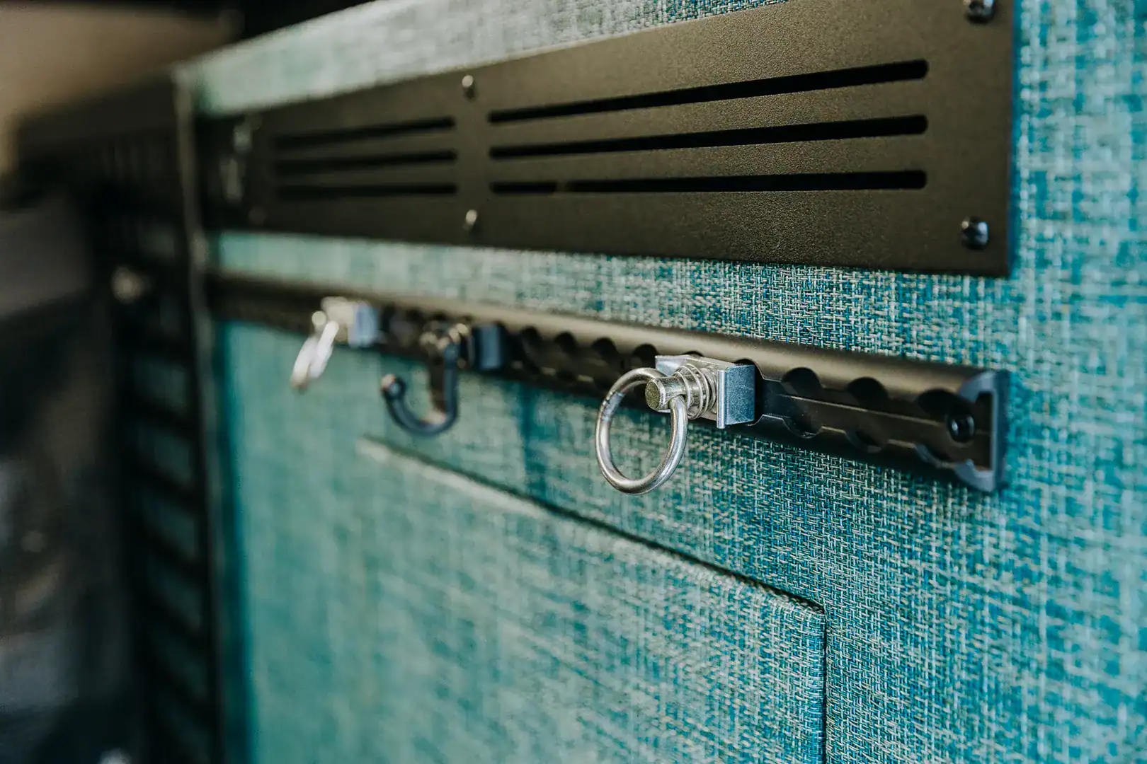 A wall-mounted gear rail with hooks on the teal textile wall of the Yama Vans Furō