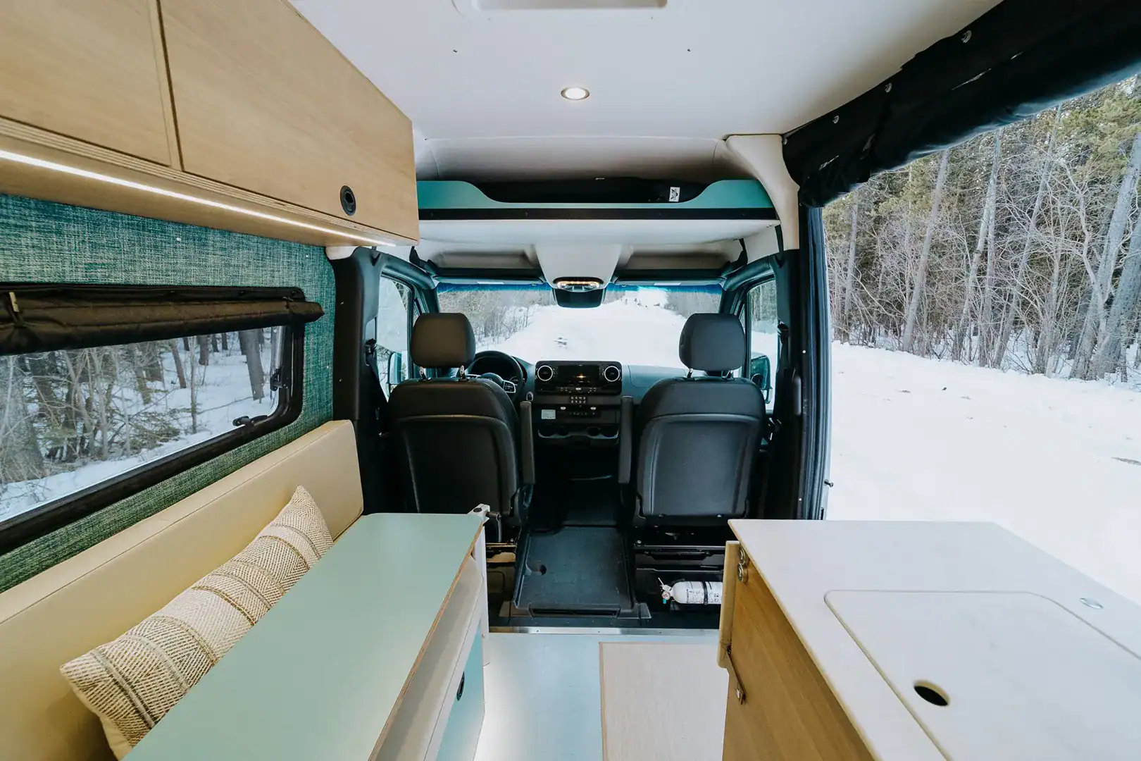 The teal and maple interior of the Yama Vans Furō with a bench seat, galley, and swivel cab seats
