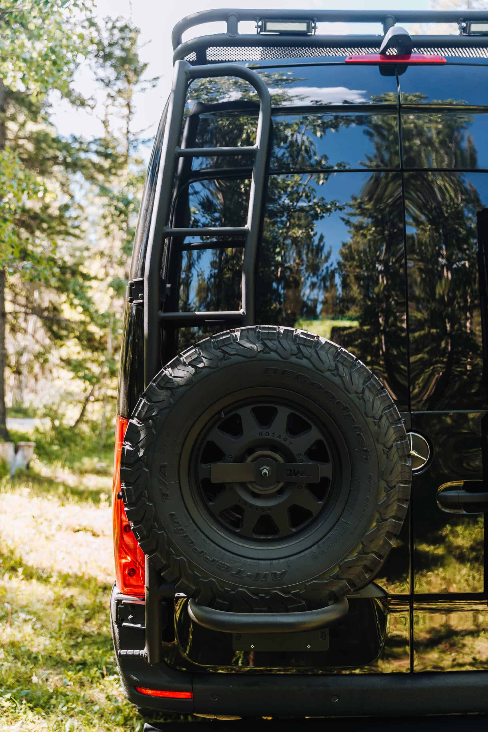 The Gatsby, a glossy black Mercedes Sprinter 170 4x4 camper van by Yama Vans with a rear ladder and full-size spare tire