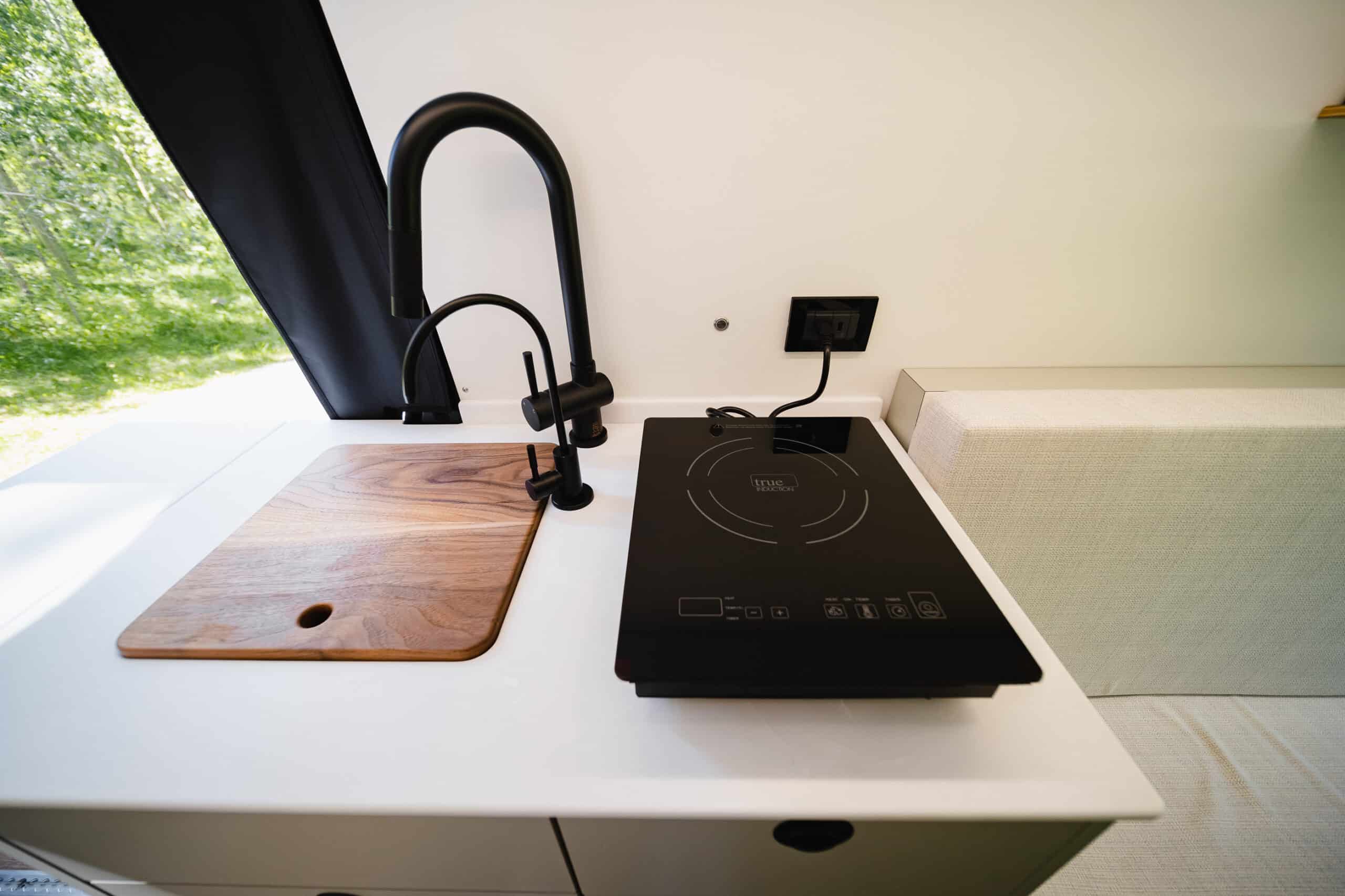 The Gatsby galley with an induction cooktop, sink, black faucet, and wood cutting board
