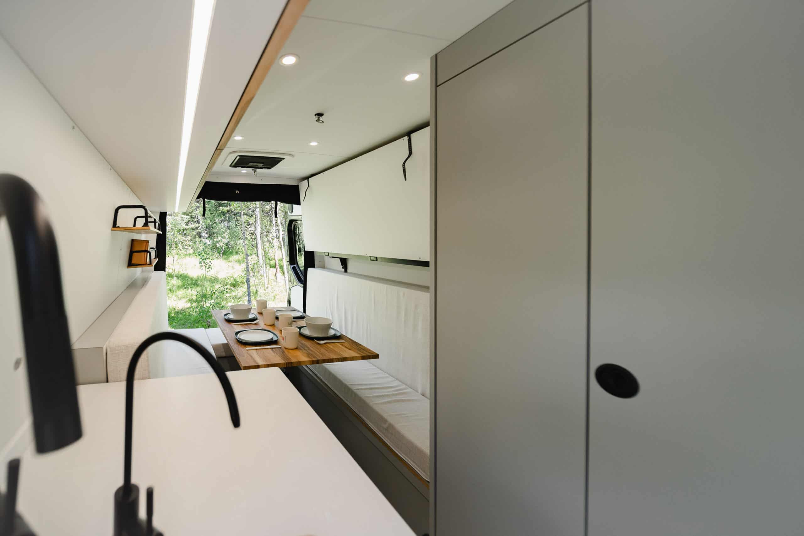 The interior of the Yama Vans Gatsby with a convertible dinette, tan leather seating, and a full-height wetroom door