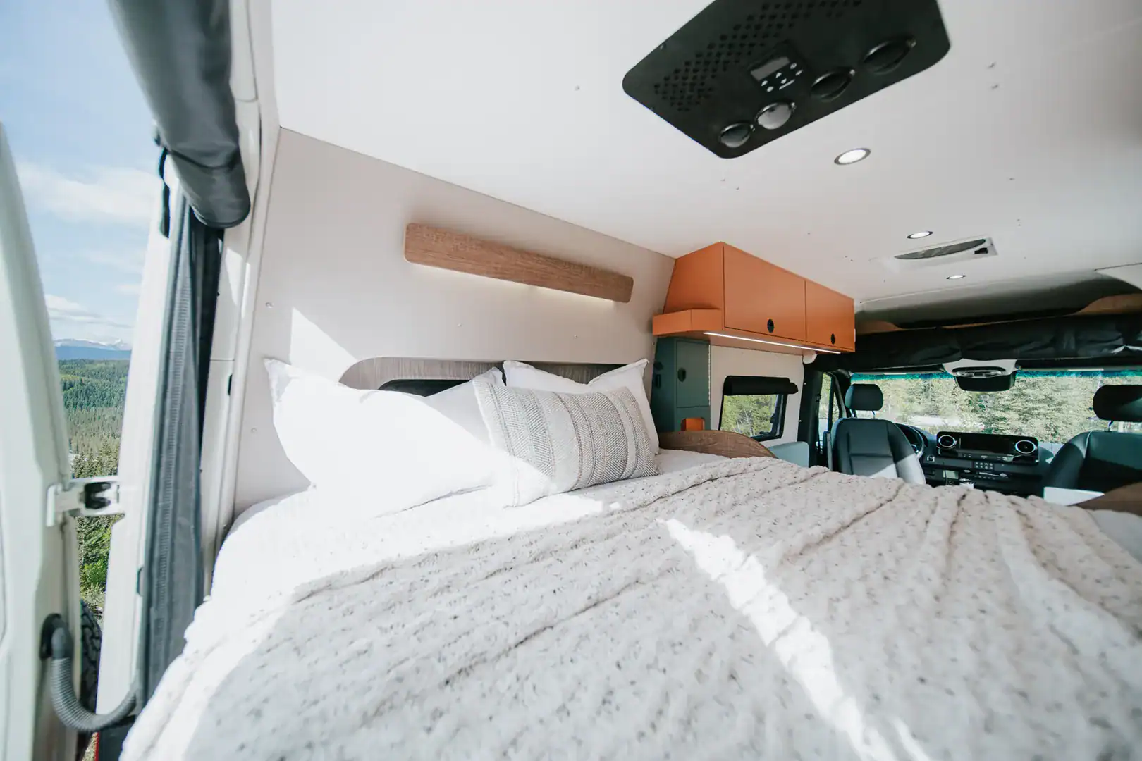 The lengthwise bed of the Yama Vans Taiyō with white bedding and warm orange overhead cabinets