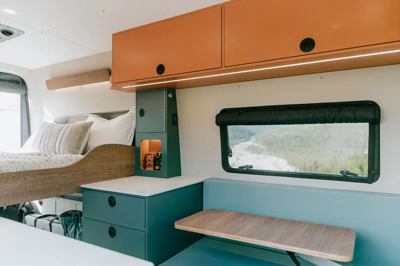 A swing-out wood table and dinette beside a window with a mountain view inside the Yama Vans Taiyō