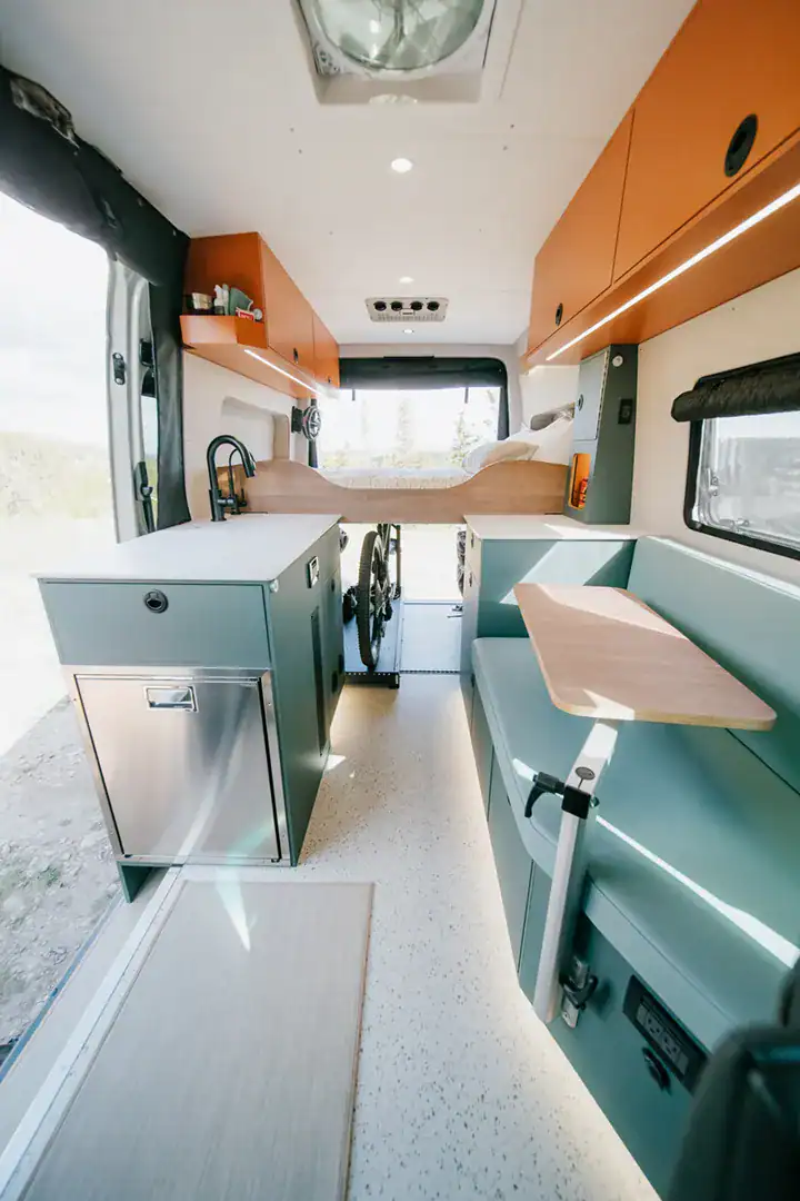 The orange and teal interior of the Yama Vans Taiyō with a galley, bench seat, and rear bed