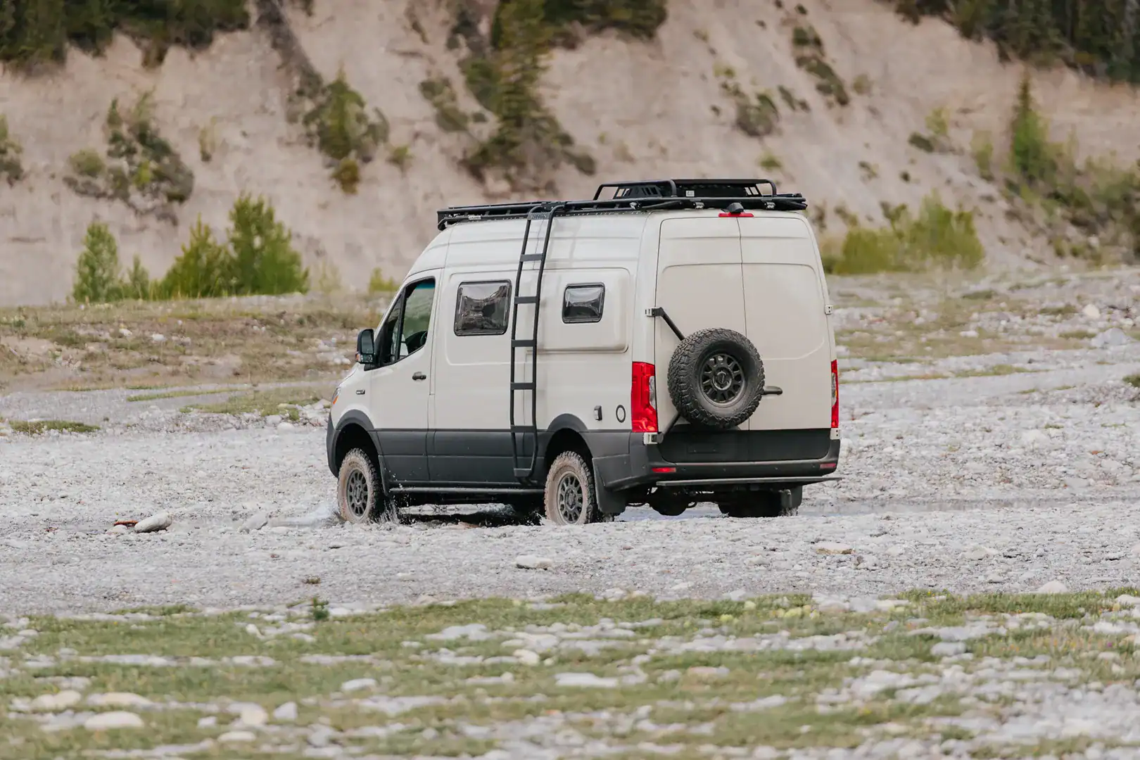 The Yama Vans Taiyō Sprinter driving through a gravel riverbed with a rear ladder and swing-away spare tire