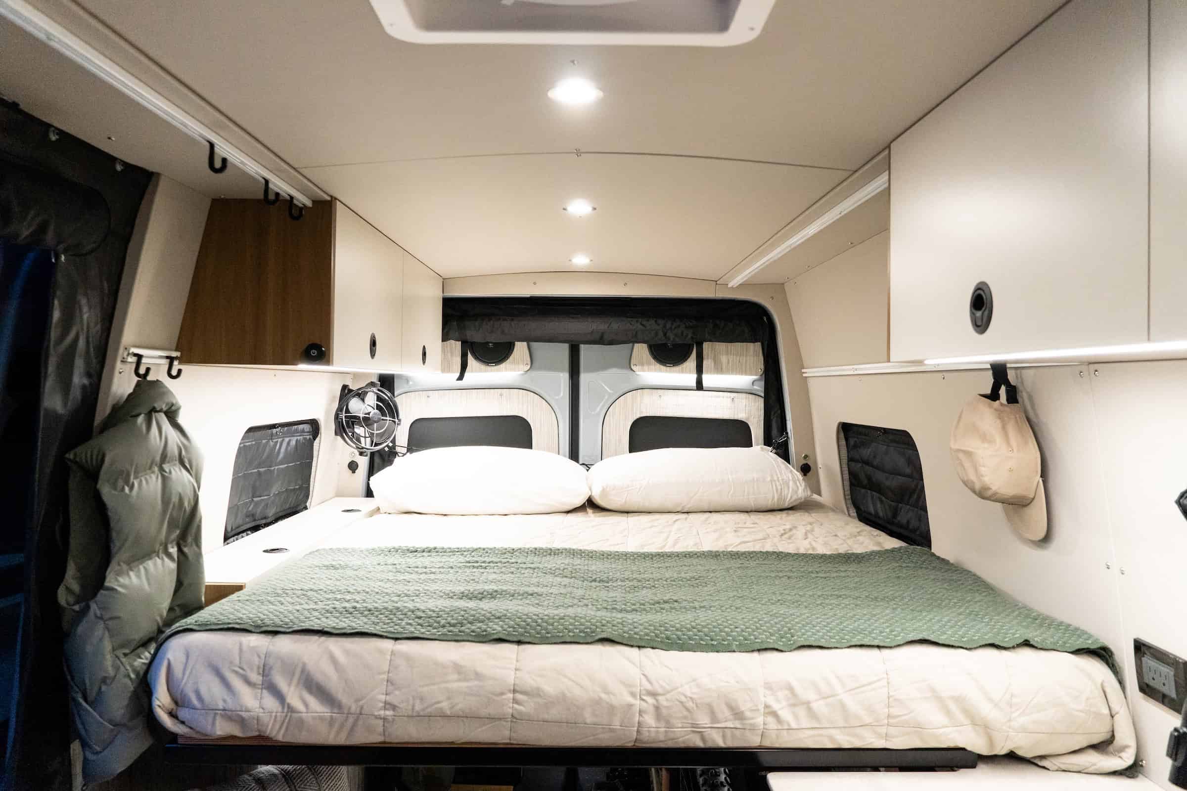 The lengthwise bed at the rear of the Yama Vans Trekka with white and maple cabinetry and two rear windows