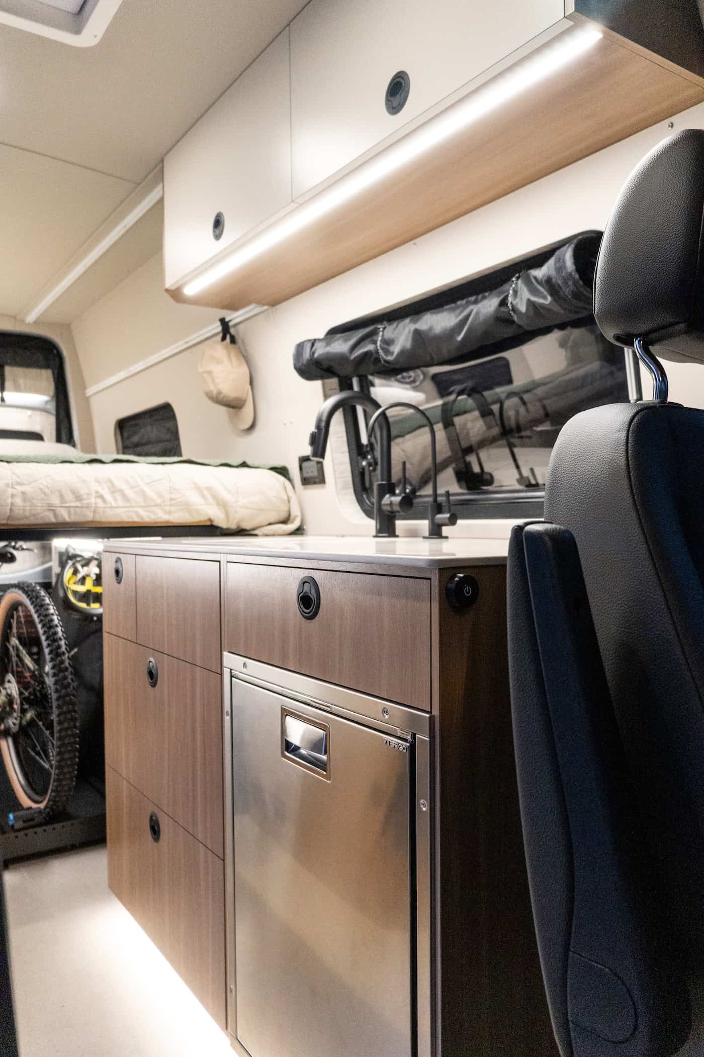 The Yama Vans Trekka galley with maple cabinets, a black faucet, and a stainless compressor refrigerator