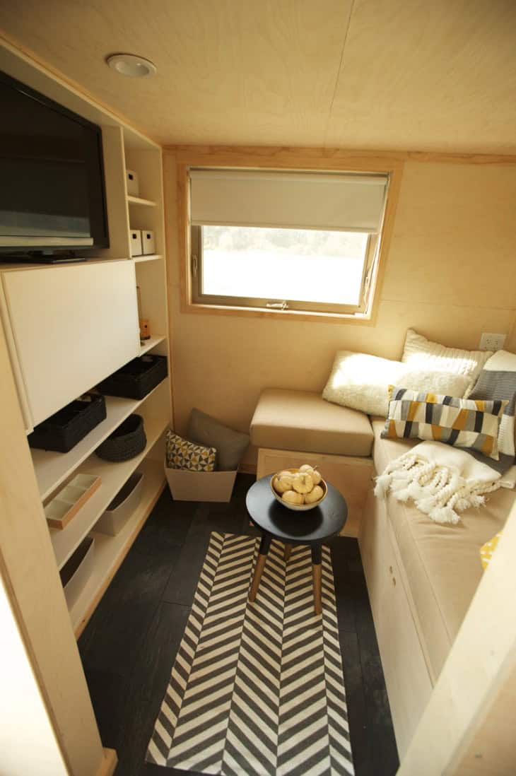 Compact tiny house interior with a comfortable sofa and large window.