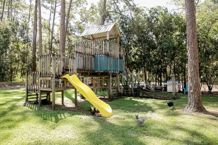 Small farm-themed playhouse with slide in a lush backyard setting.