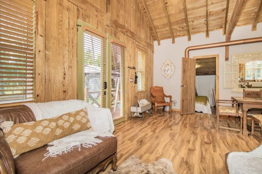 Cozy farm cottage living room with wooden walls and large windows.