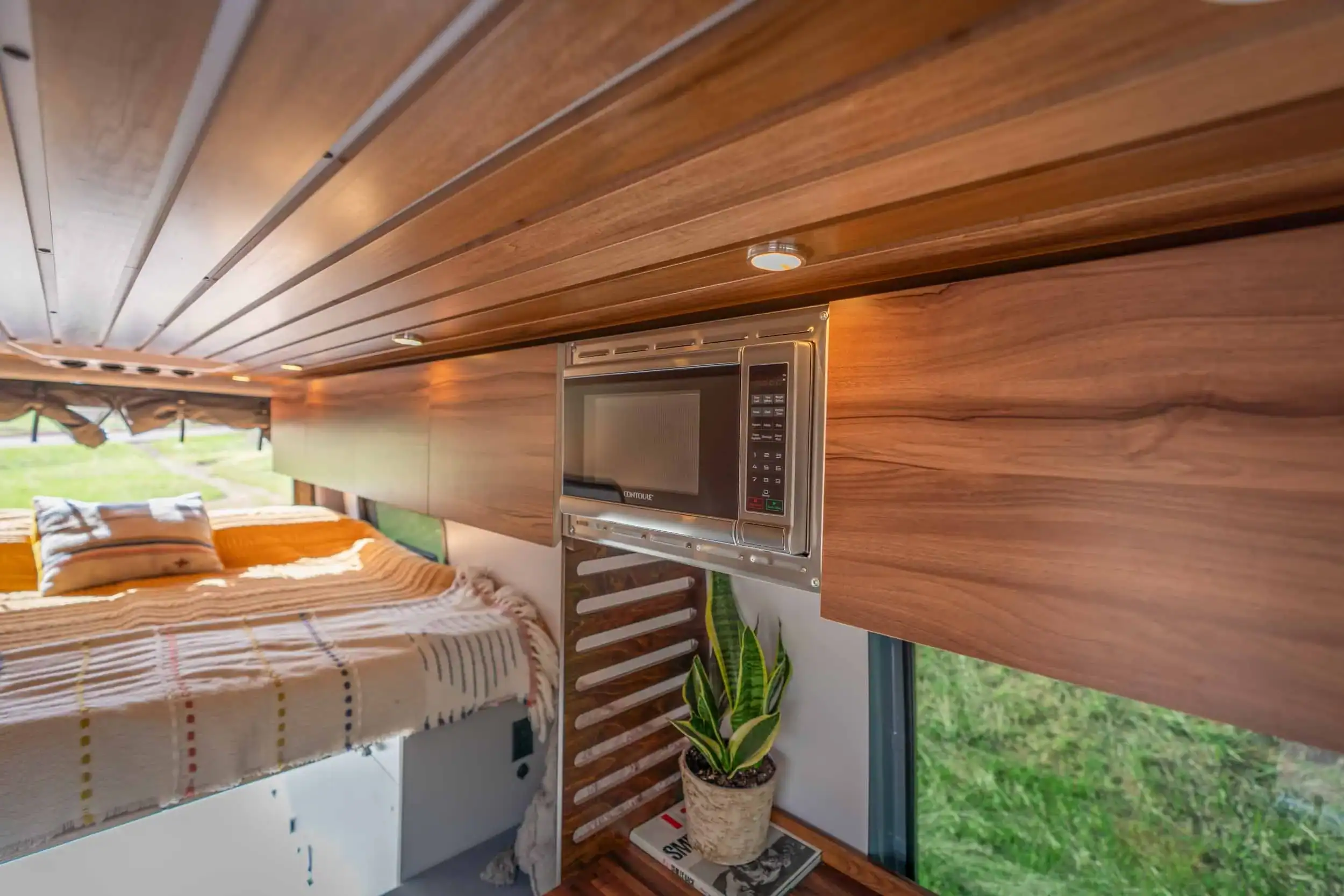 Compact tiny house interior featuring a wooden ceiling, built-in microwave, and cozy sleeping area w.