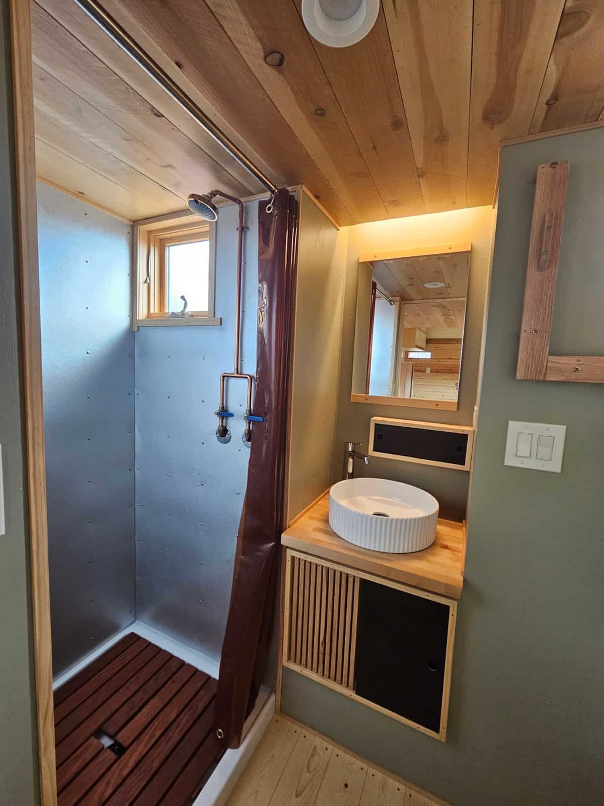 Bathroom with metal shower, exposed copper pipes, redwood shower plank, and a white vessel sink on a wood vanity