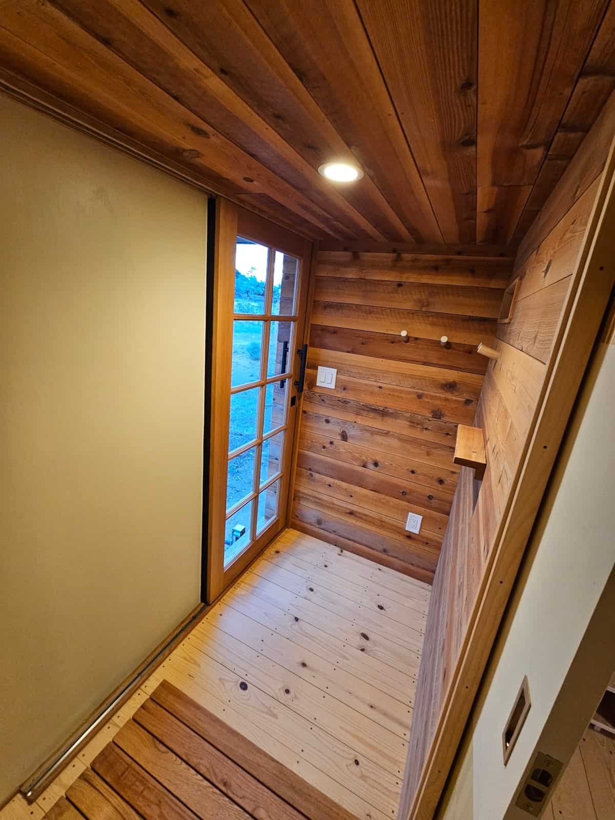Japanese-style genkan entry vestibule with spruce floors, cedar walls, a slatted shoe mat, and a 12-pane glass door