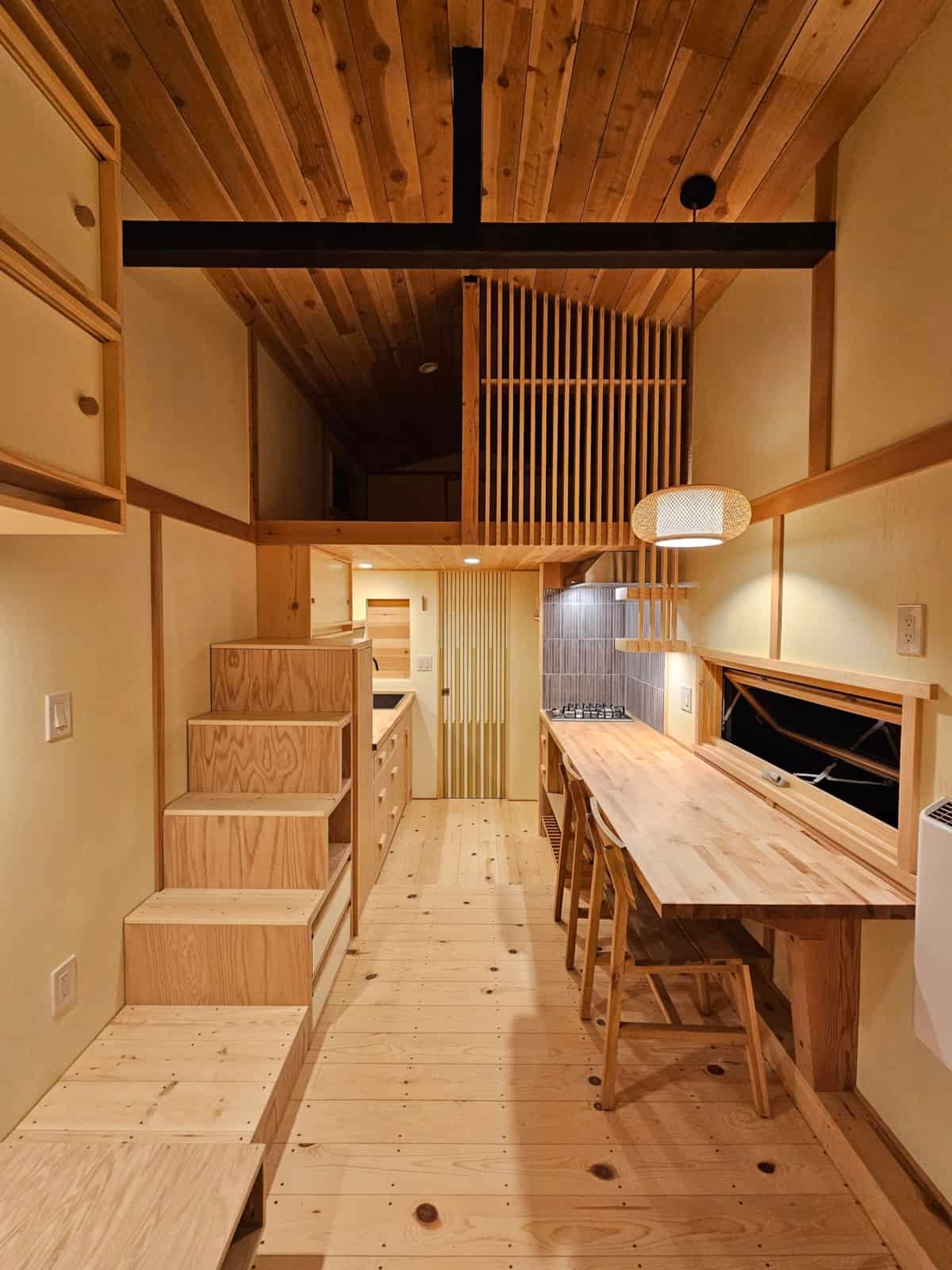 Living space with tansu storage stairs, dining counter, spruce floors, and a slat screen on the sleeping loft