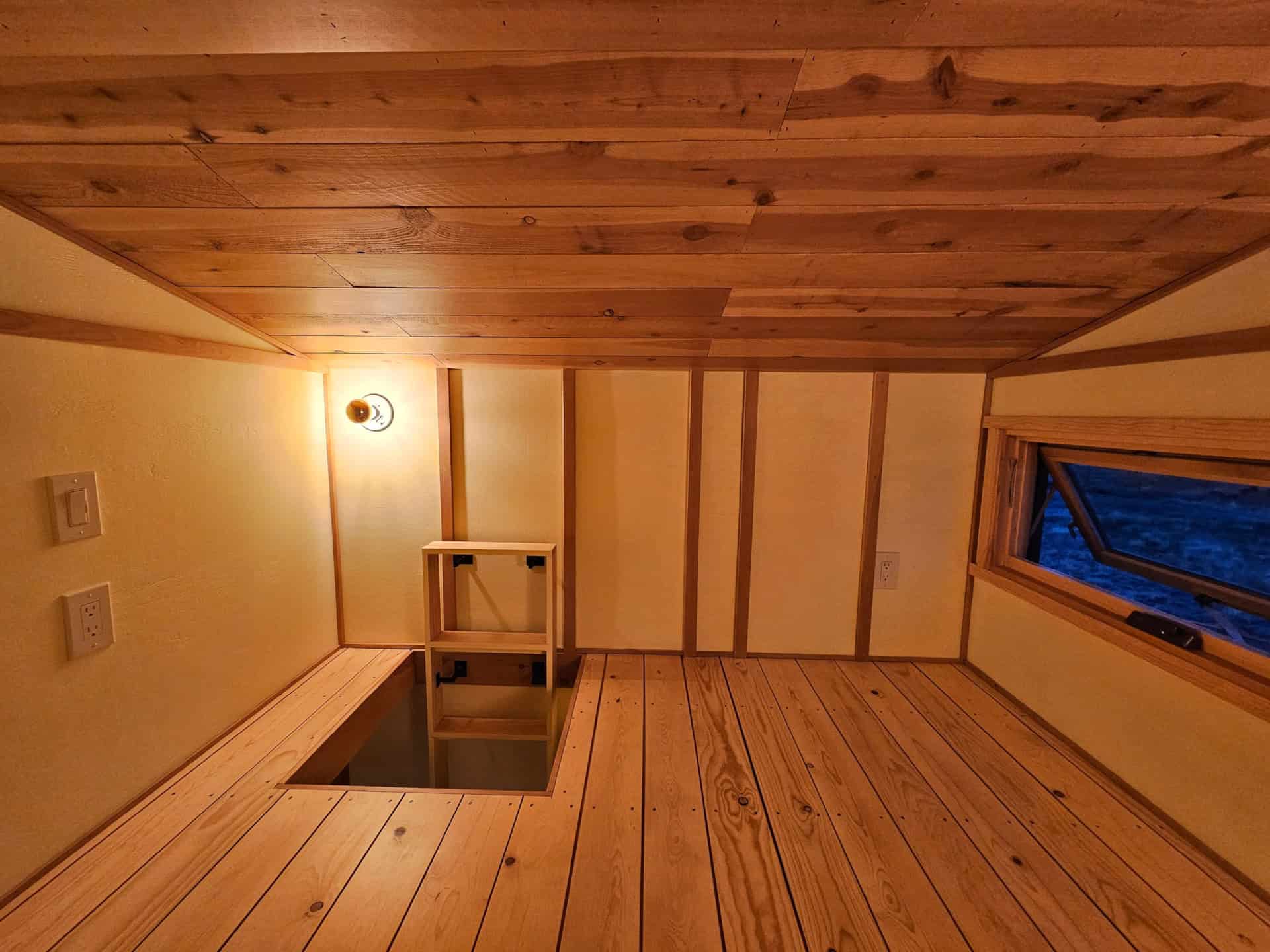Sleeping loft with spruce plank floor, cedar-plank sloped ceiling, timber-framed walls, and an awning window