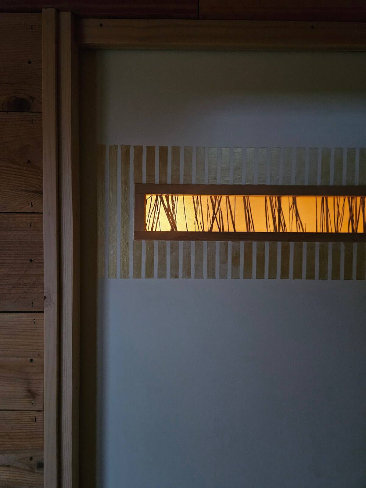Backlit tokonoma display alcove with reed silhouettes, warm glow, and a timber post
