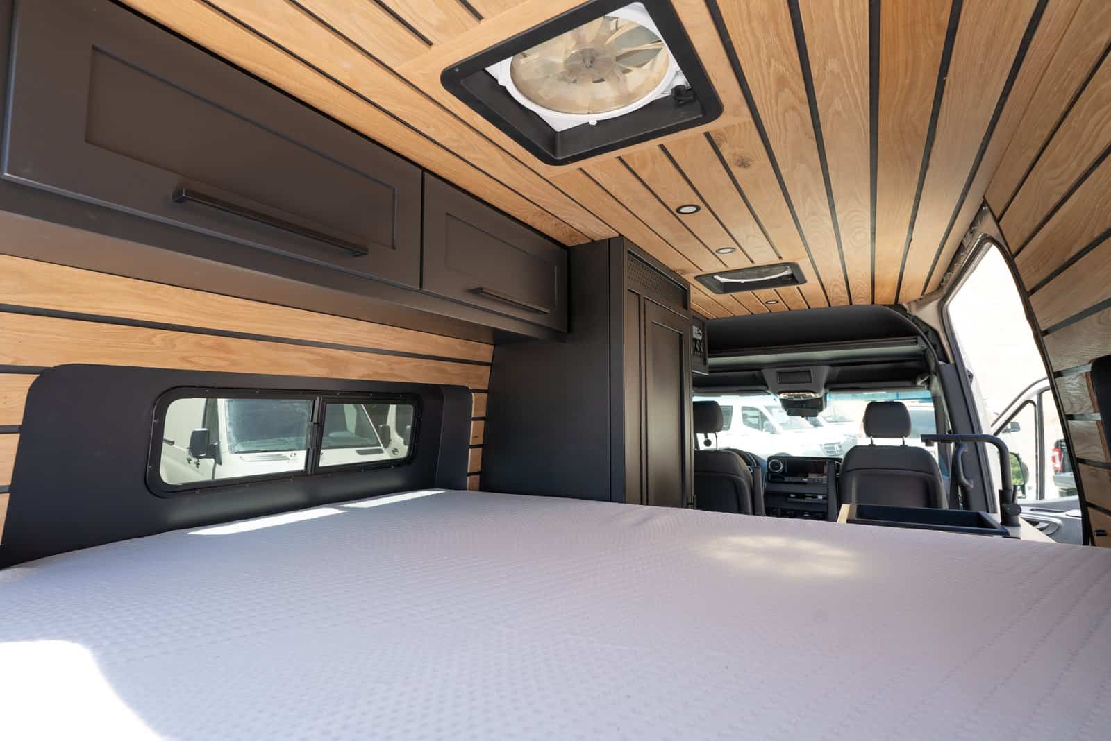 View from the bed looking forward through the van to the cab, with overhead cabinets and a roof fan