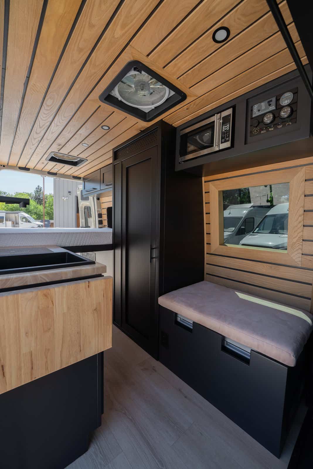 Bench seat with a pink cushion under a wood-framed window, with a microwave and control panel above