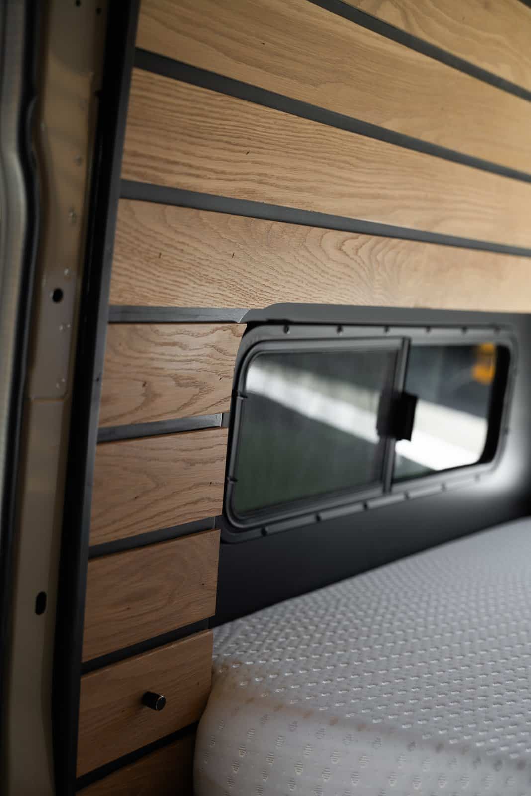 Close-up of a window set into the molded body flare beside the mattress, with wood slat walls above