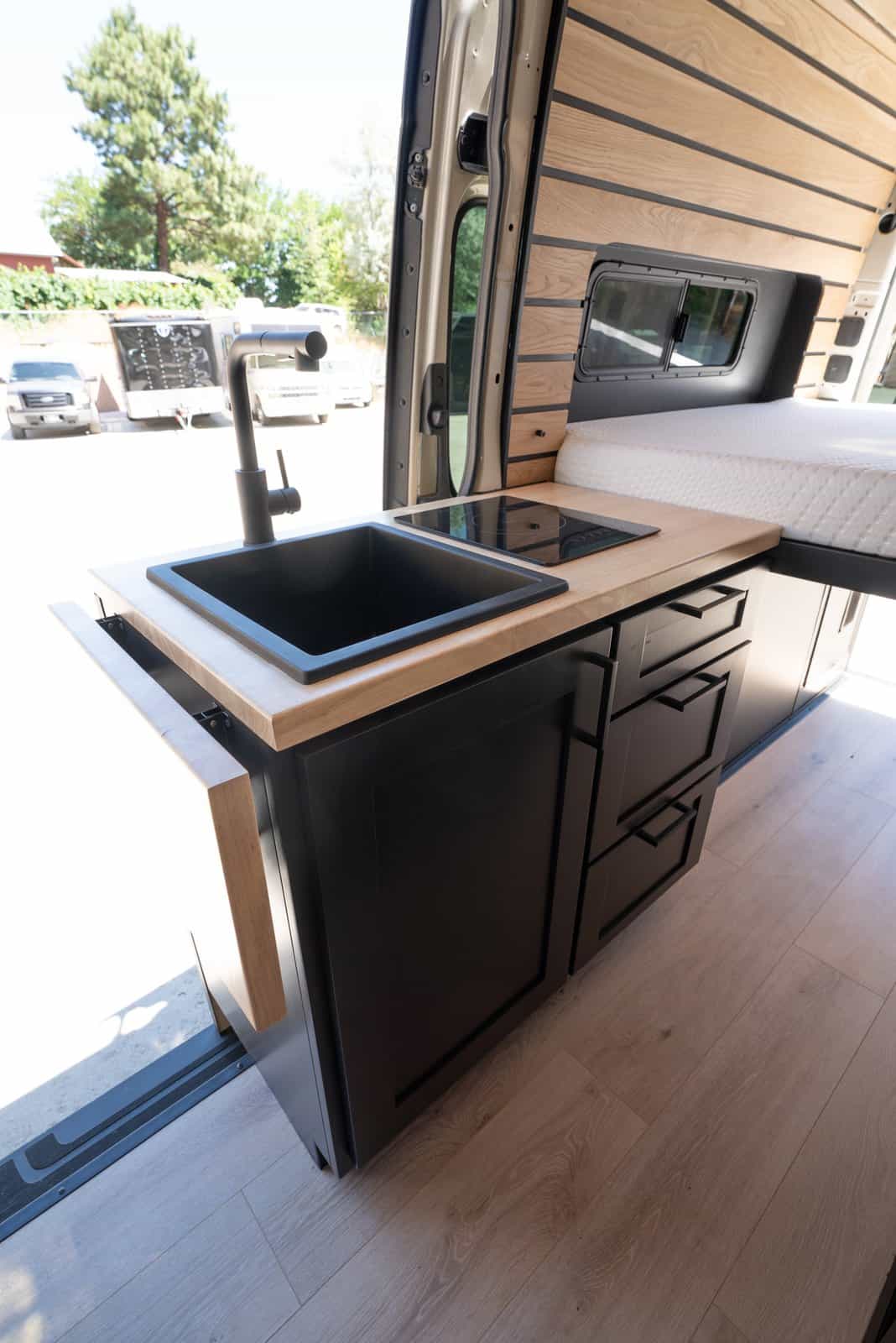 Galley counter with a black sink and faucet, induction cooktop, and stacked black drawers