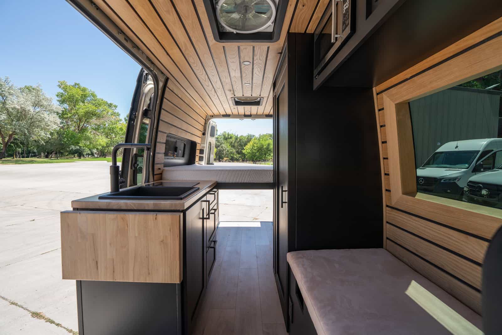 View down the length of the van past the galley and bench seat to the bed at the back, with the side door open