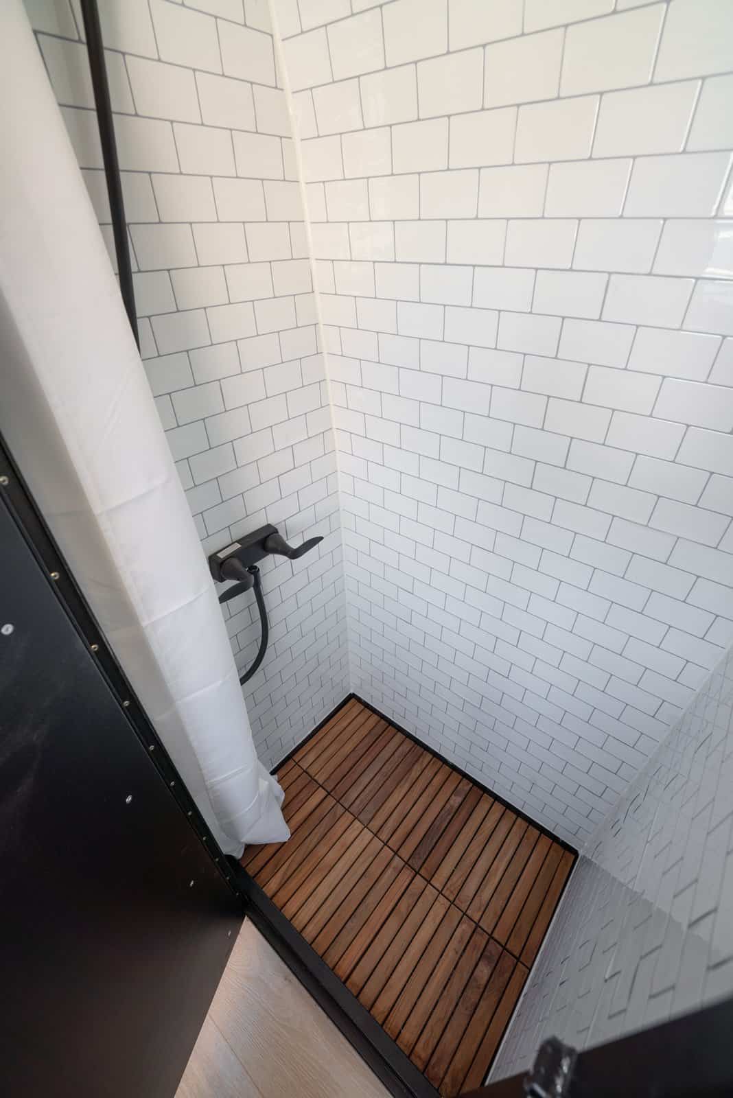 Close-up of the shower's teak floor and white subway tile walls