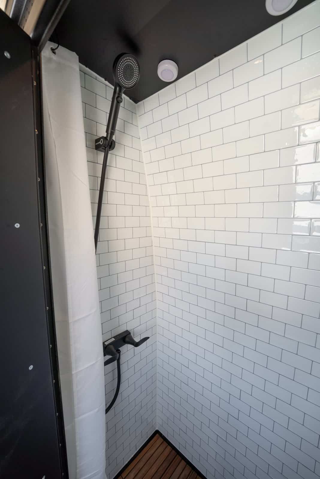 Indoor shower with white subway tile, a black handheld shower head, and a teak floor