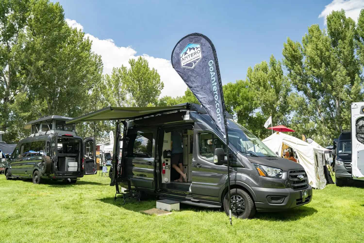 Charcoal Ford Transit with awning open on the grass at Adventure Van Expo, North Lake Tahoe, Antero Adventure Motors flag beside it
