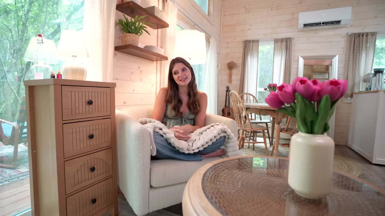 Annie sitting in a white armchair in the living area of her light-wood tiny house