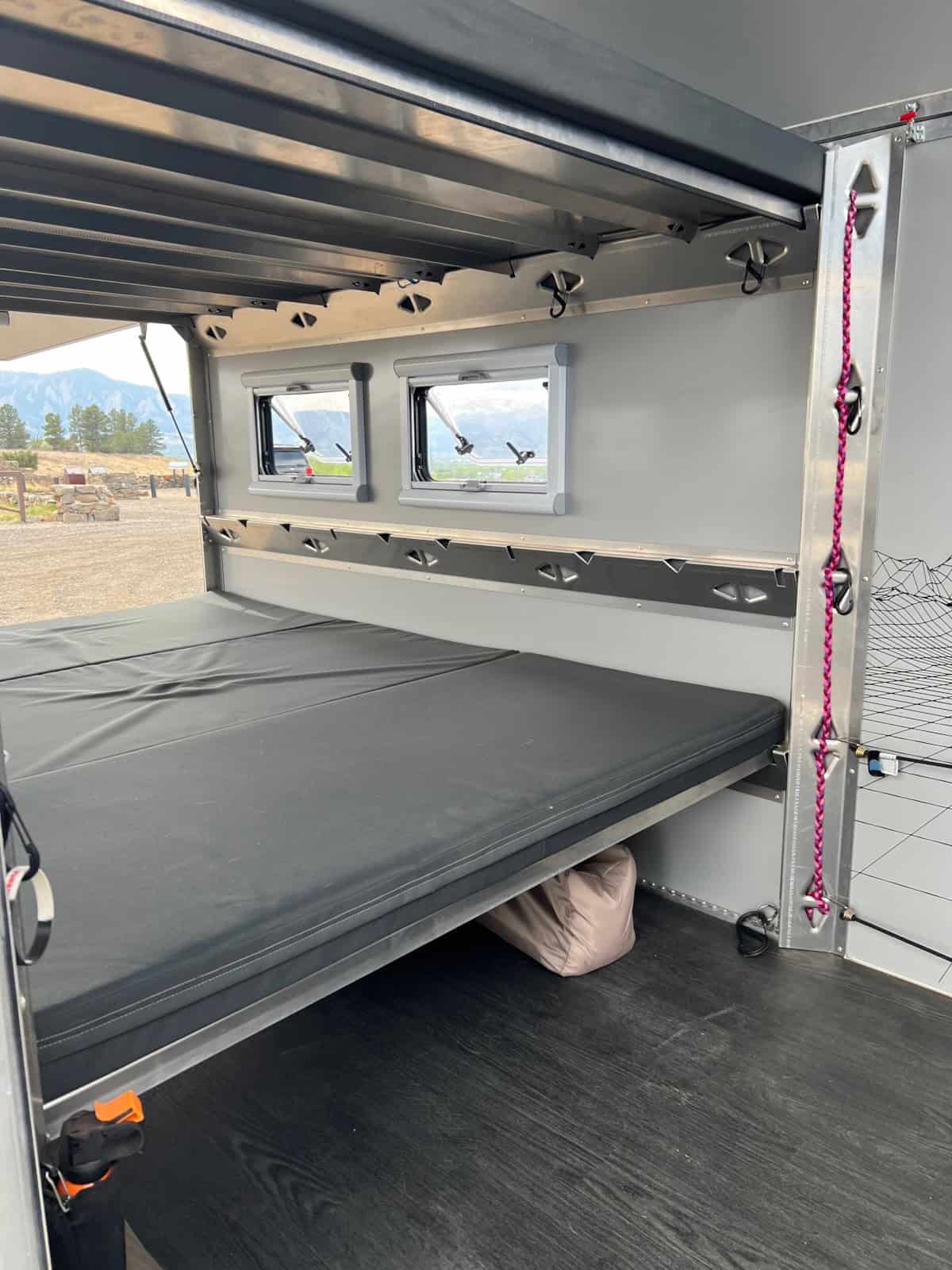 Interior stacked queen bunks on aluminum frames with dark-gray mattresses and open side windows