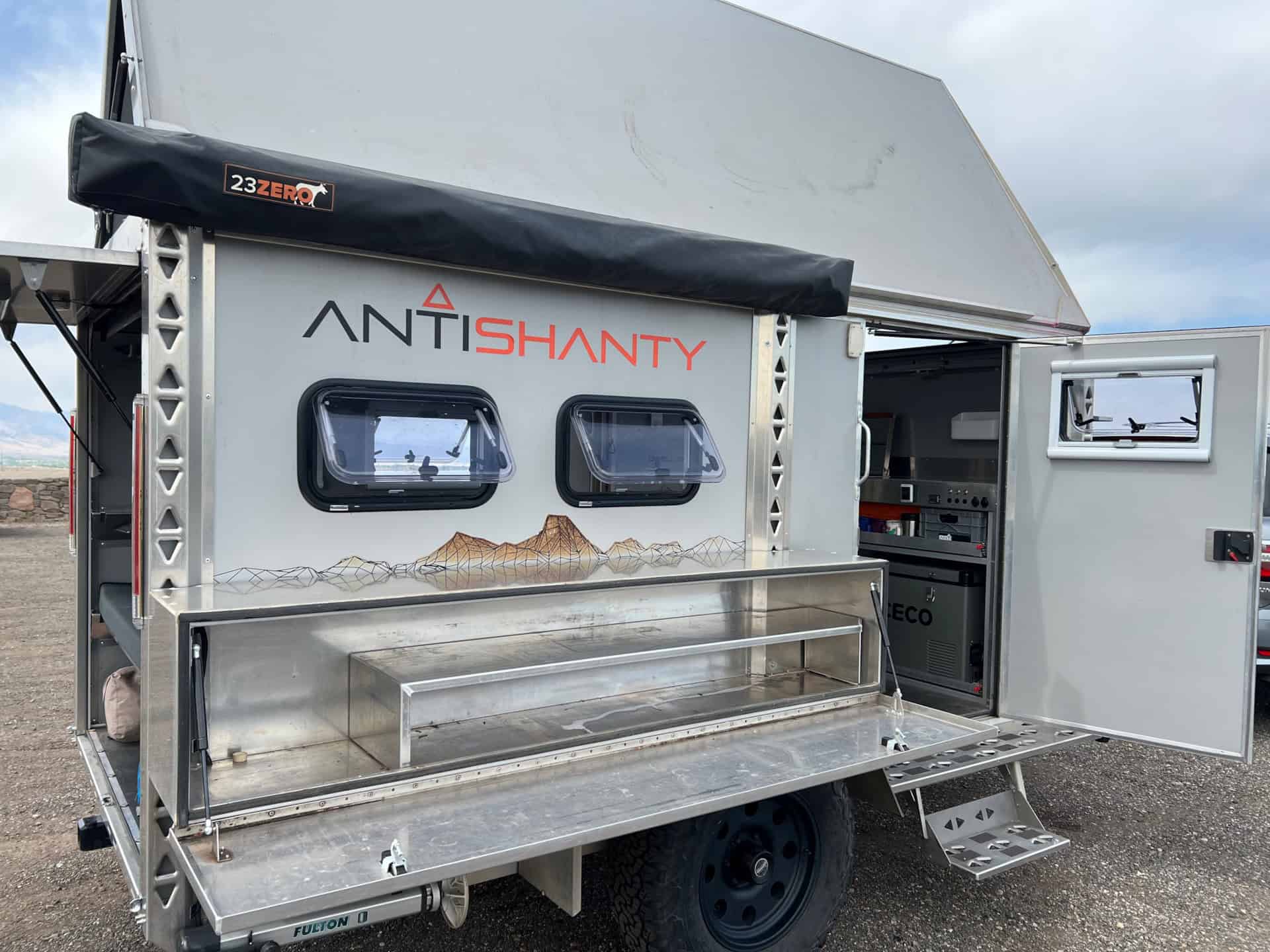 Camp-mode passenger side with A-frame up, kitchen box open, side door open, and ICECO fridge visible inside