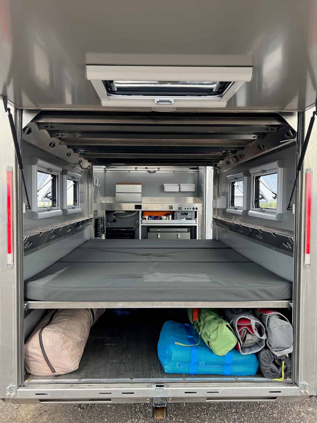 Open rear hatch looking in at the bunk platform, under-bed gear storage, and kitchen at the far end