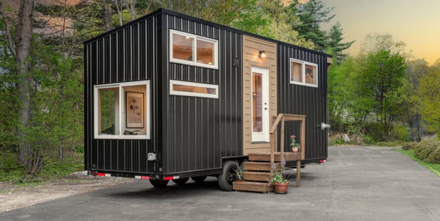 Backcountry Honey Bee exterior: black corrugated siding, honey-wood entry accent, white-trimmed windows, dual-axle trailer, wood steps