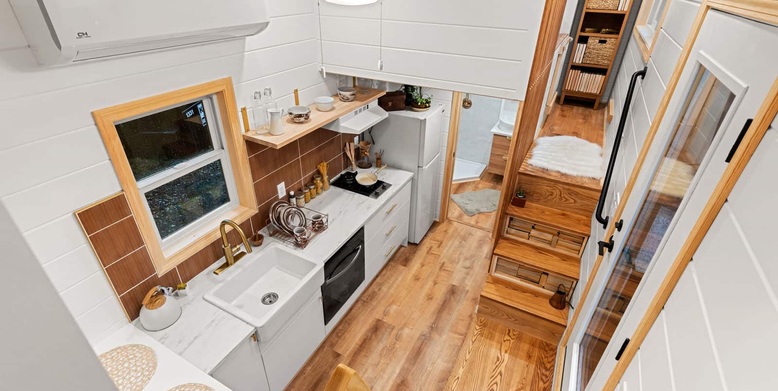 Honey Bee kitchen: farmhouse sink, gold faucet, cooktop, white drawers, wood shelf toward loft stairs
