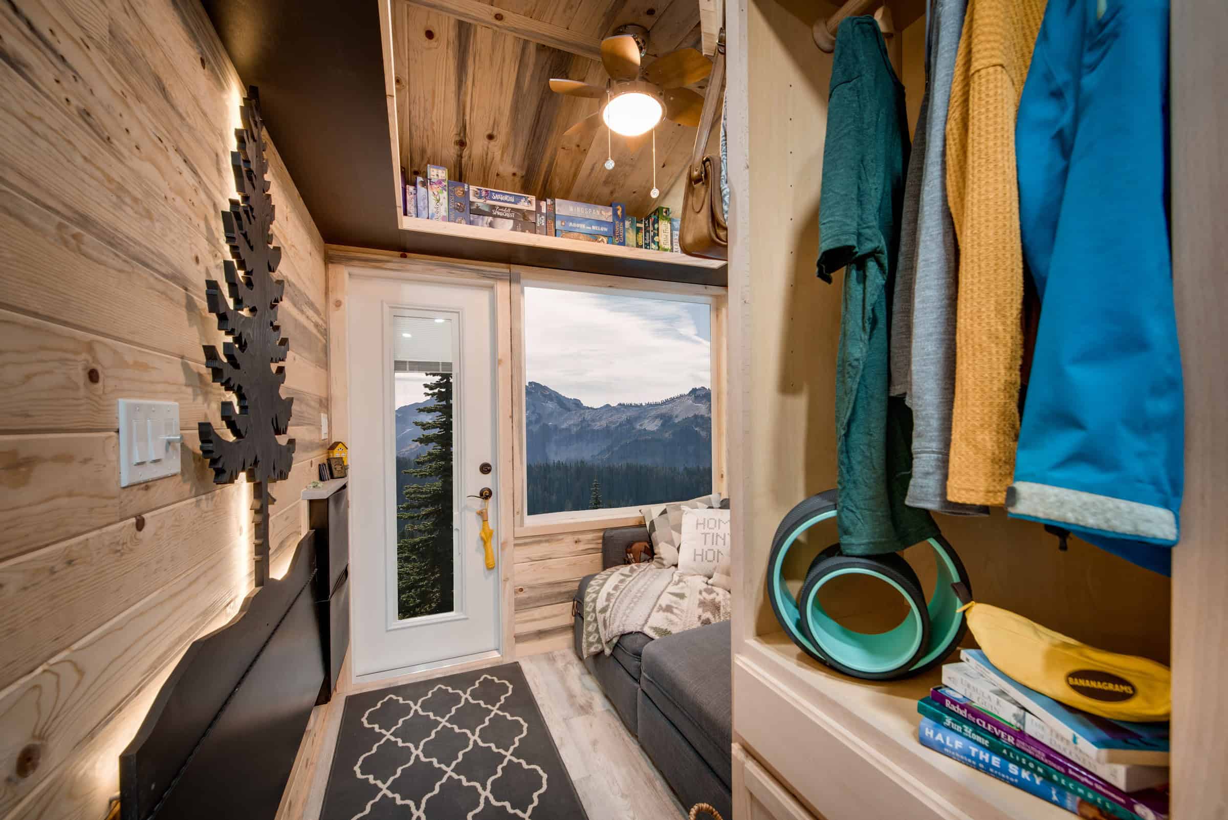 Traveler entry: beetle-kill knotty pine walls and vaulted ceiling, white glass door, grey sleeper sofa under a mountain window, backlit tree on the wall