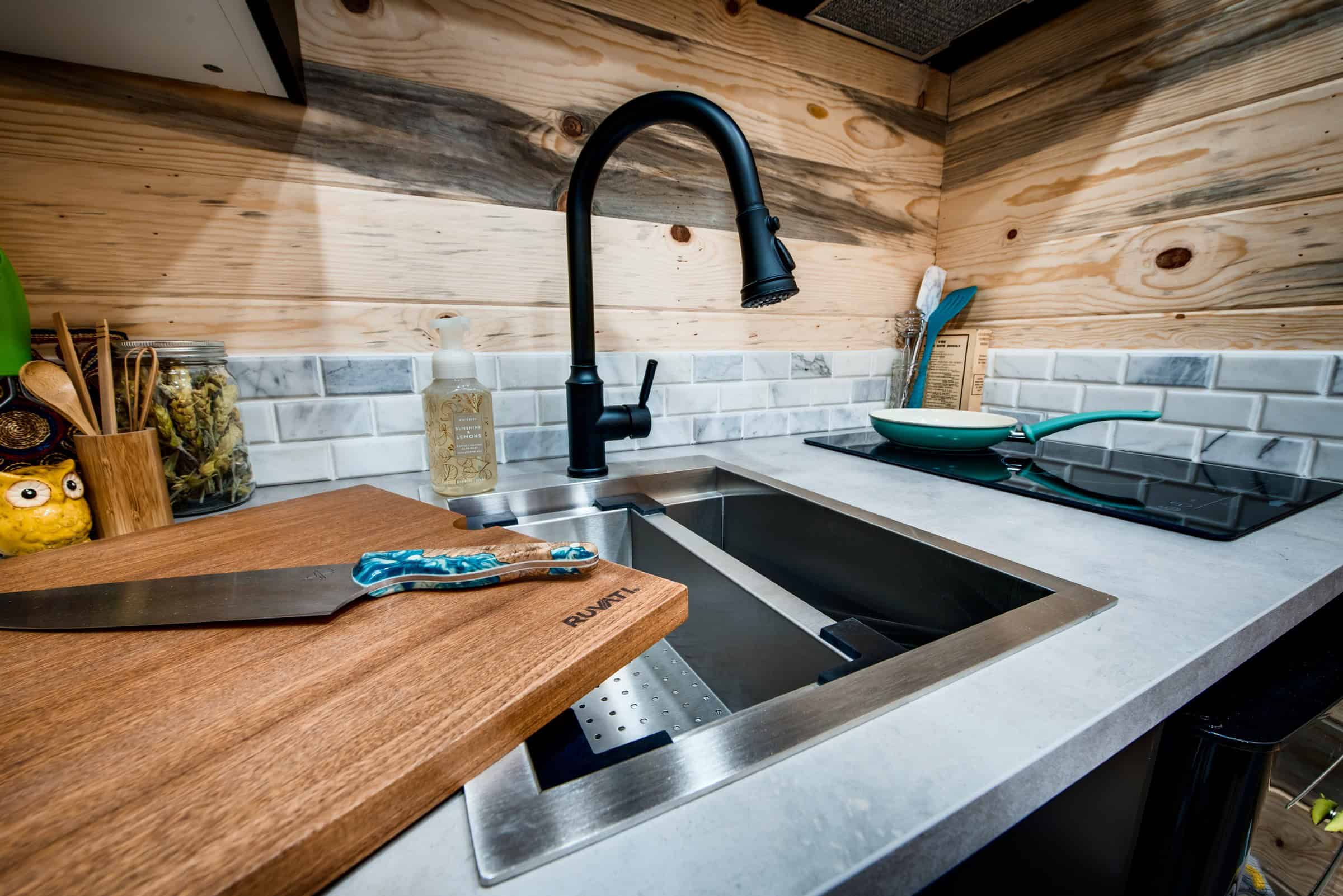 Traveler kitchen: stainless steel workstation sink with a wood board insert, pull-down faucet, two-burner electric cooktop, knotty pine walls, laminate counter