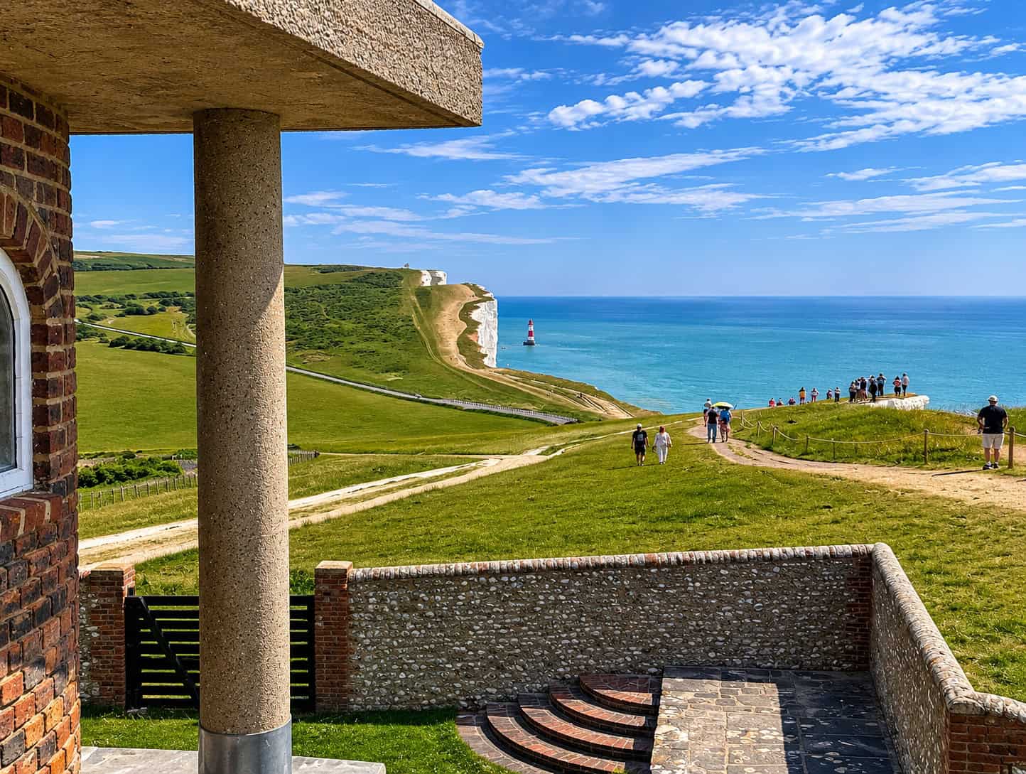 View east from Belle Tout: green clifftop, walkers on the coastal path, white chalk cliffs and blue sea