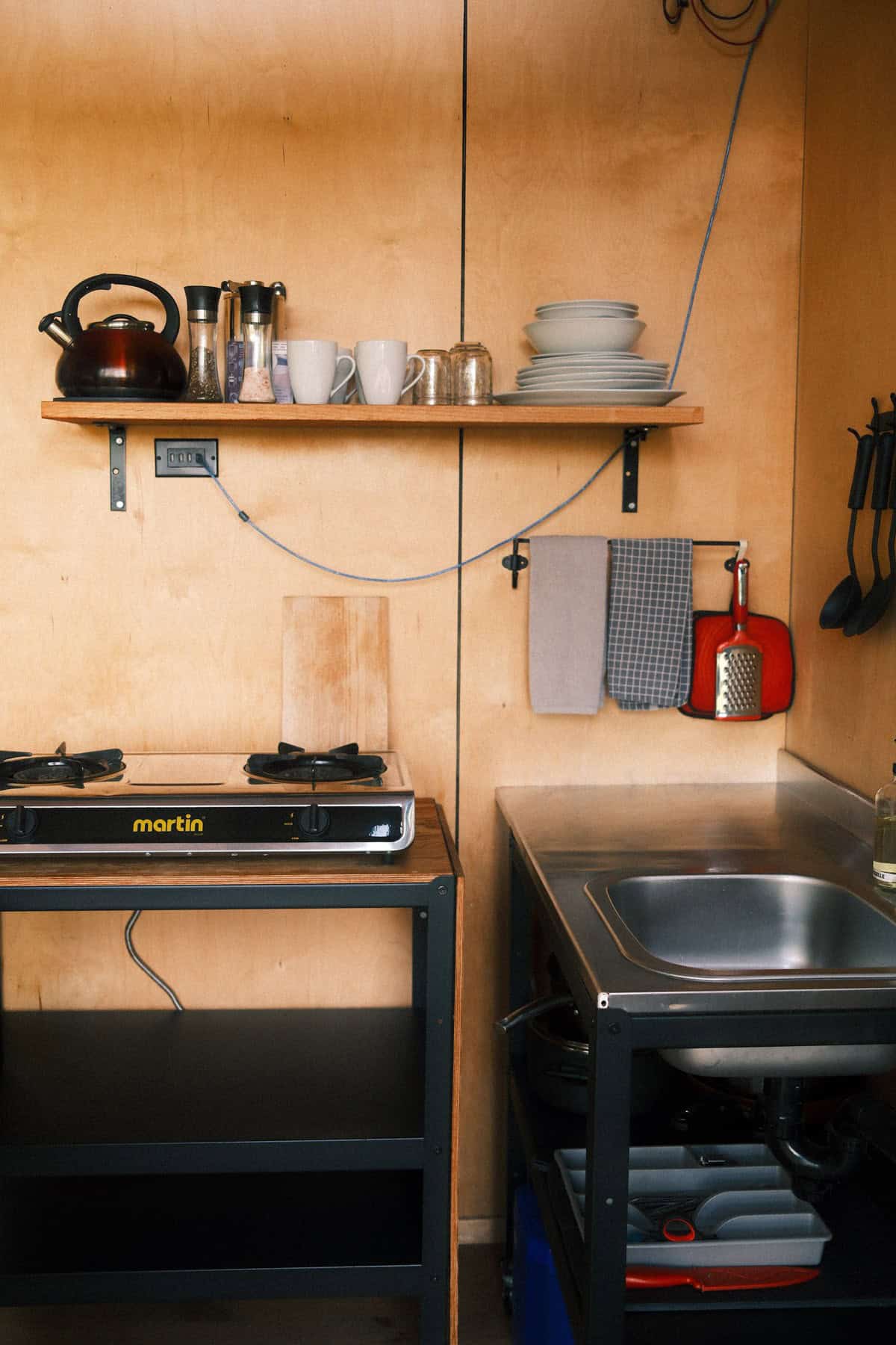 Kitchenette with two-burner stove, sink, and open shelving inside BESIDE LAO Canopée