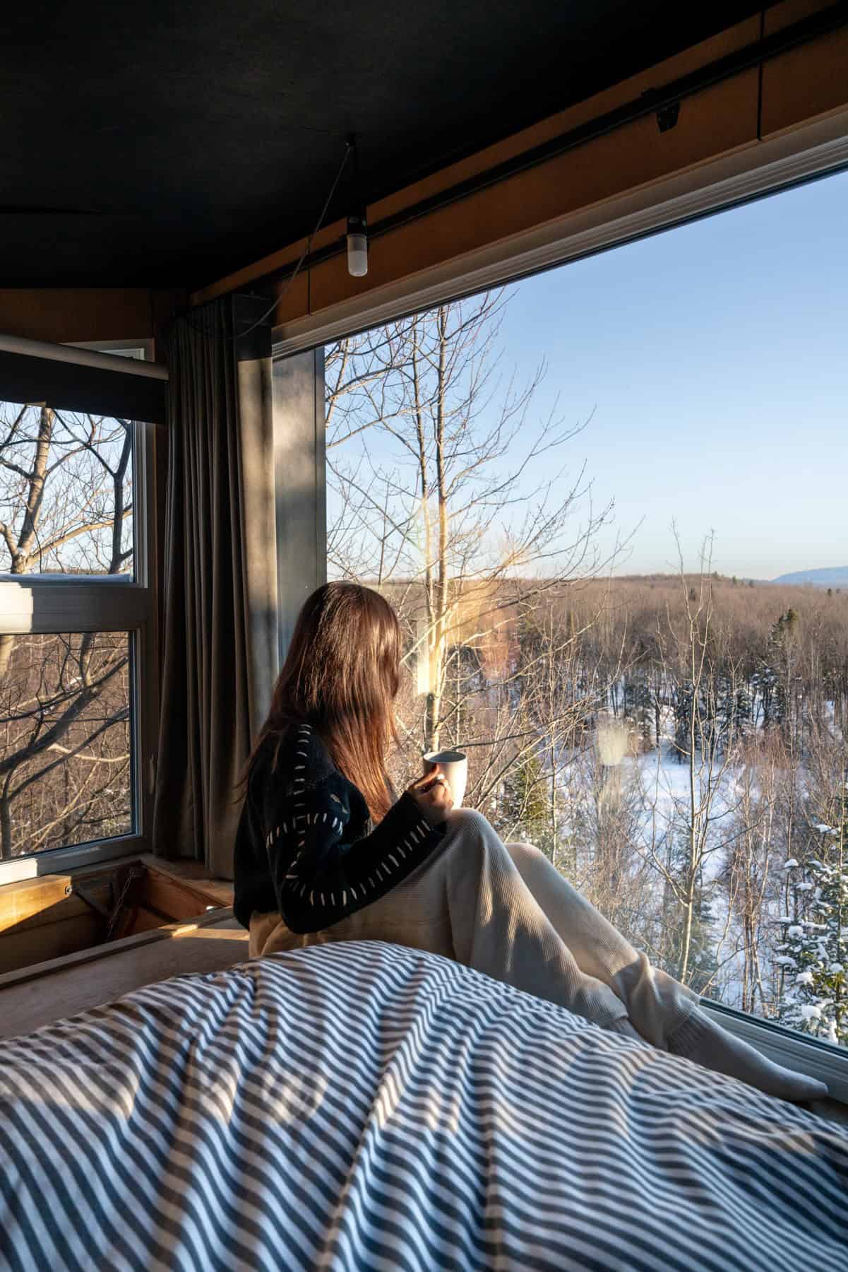 Guest at floor-to-ceiling window looking over snowy forest inside BESIDE LAO Canopée