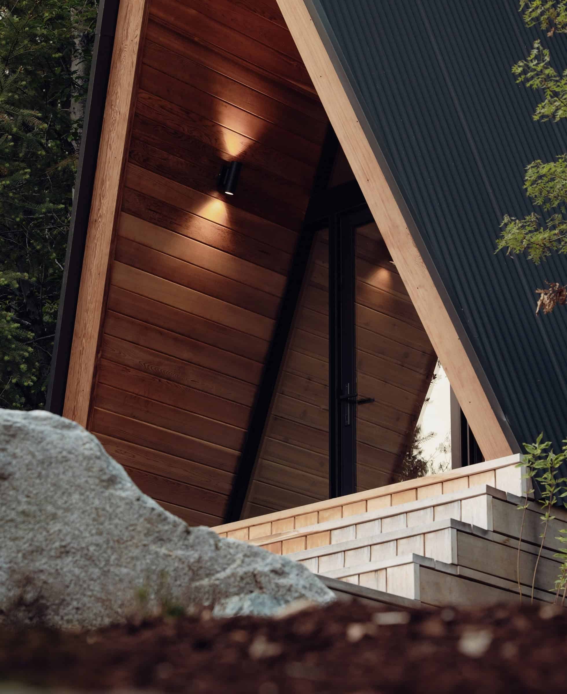 System 00 entry close-up: black metal A-frame, wood-lined porch, wall sconce