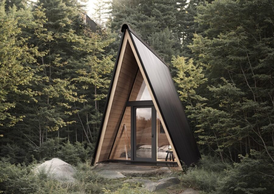 System 00 prefab A-frame: black metal exterior, full glass front, warm interior light in the forest