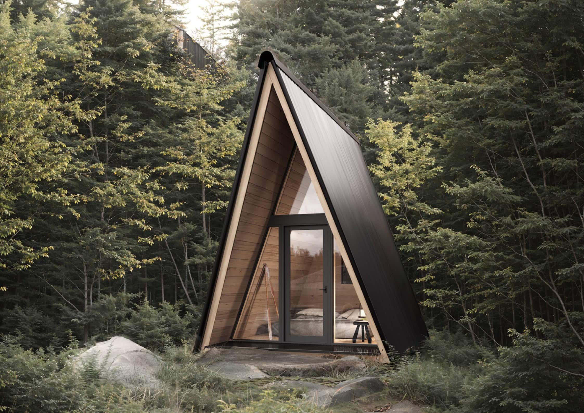 System 00 prefab A-frame: black metal exterior, full glass front, warm interior light in the forest