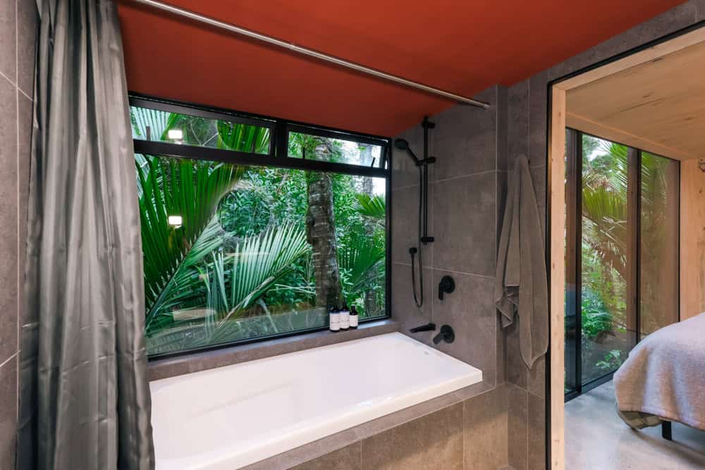 Dark-tile bathroom with a white tub aimed at a nikau in the window